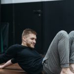 Young man performing a stretching and relaxation exercise on a gym floor.