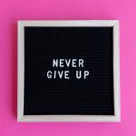 A framed letter board with 'NEVER GIVE UP' on a vibrant pink background.